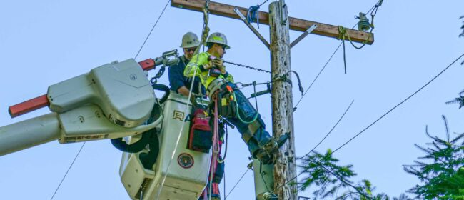 Line crew in a crane bucket drilling into the utility pole