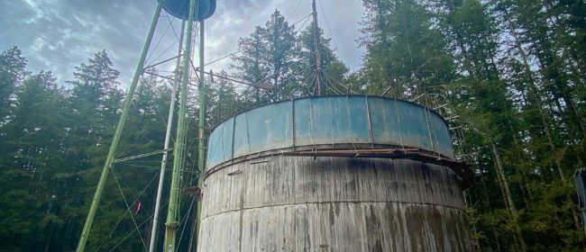 A photo of the new Quilcene concrete water tank still partial led in forms with the old standing metal water tank behind it.